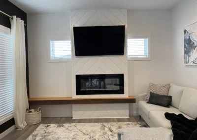 Modern living room with chevron accent wall, floating wood mantel, linear fireplace, and wall-mounted TV by Saskatoon basement developer Axium Interiors.