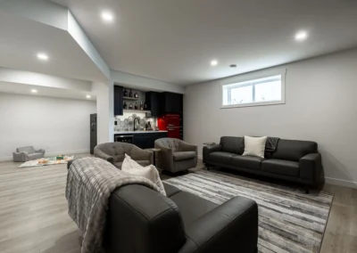 Modern basement with leather sofas, wet bar, red fridge, and wood-look flooring by Saskatoon basement developer Axium Interiors.