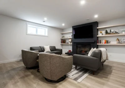 Modern basement living room with black shiplap fireplace, floating shelves, leather seating, and swivel chairs by Axium Interiors Saskatoon.